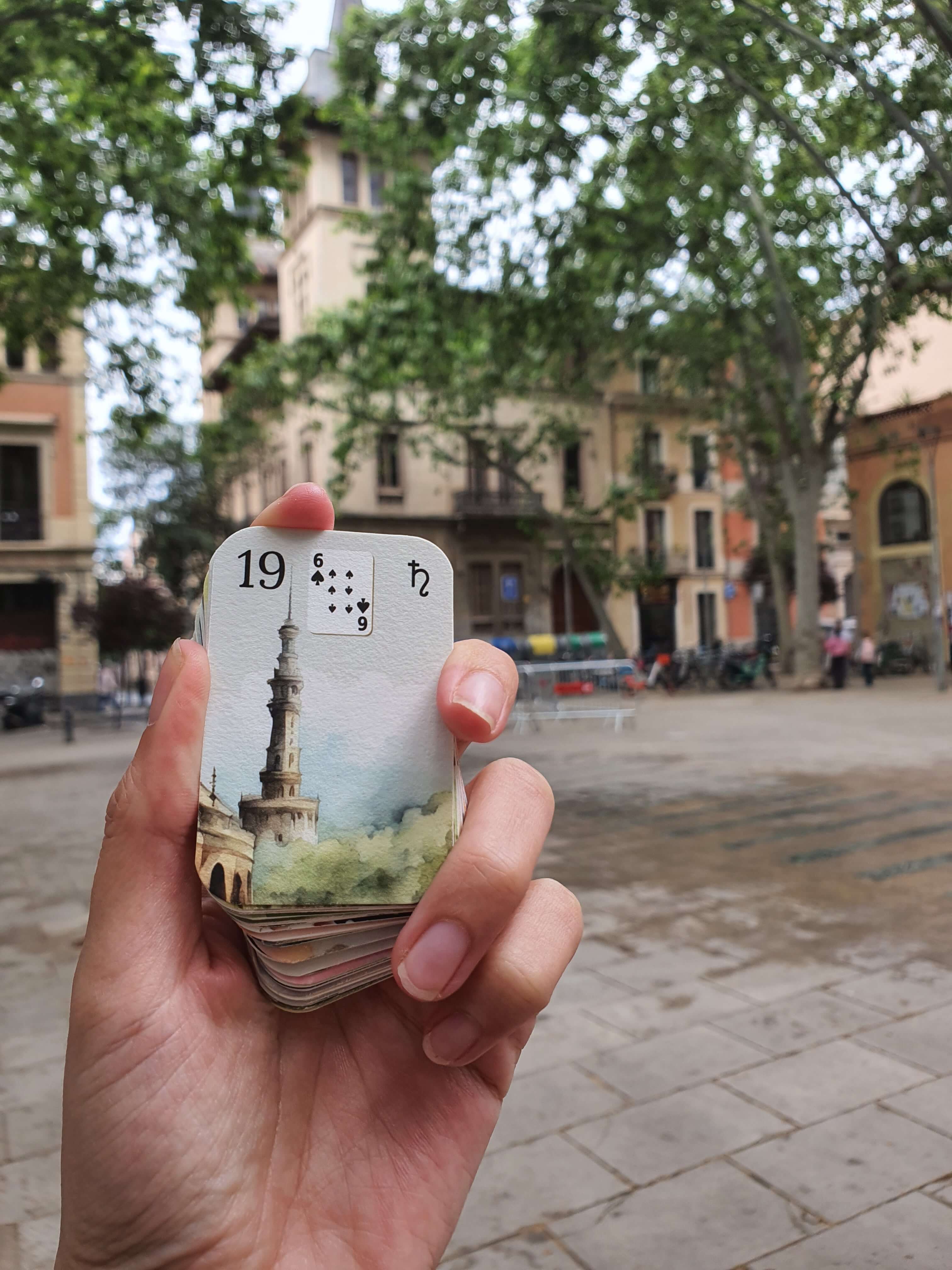 Mini deck aquarelle Petit Lenormand tenu dans la main devant une place arborée